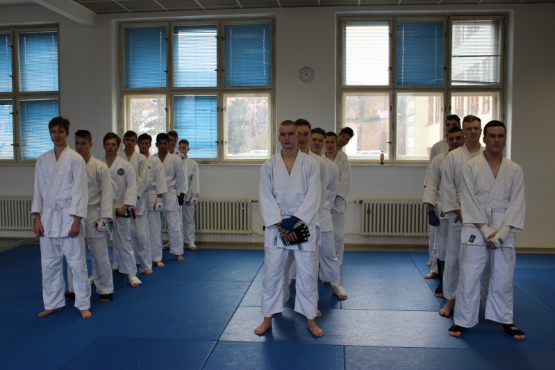 Žáci v bílých kimonech nastoupení v tělocvičně před turnajem v karate.